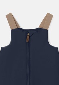 Marineblå ermeløs jumpsuit med beige stropper, med en glidelås nedover midten og et lite tre-glidelåsdrag for detalj.