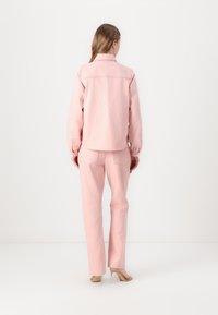 Pink denim jacket and matching trousers, both with a smooth texture and casual fit. The jacket features a collar and buttoned cuffs.