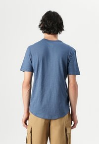 Blauw T-shirt met korte mouwen en een ronde hals, gemaakt van een textuurstof, met een gebogen zoom, weergegeven vanuit de achterkant.