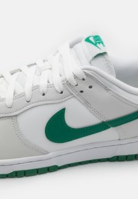 Sapatilha Nike branca e verde com cadarços brancos, logótipo swoosh verde de lado e marcação verde na língua, sobre um fundo branco.