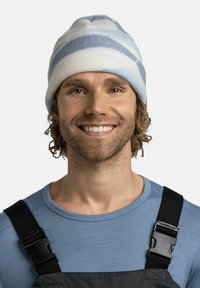 Gorro de rayas azul claro y blanco, hecho de tela suave, con un ajuste ceñido. El hombre lo lleva con una camiseta de manga larga azul y un overol oscuro.