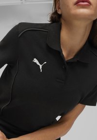 Zwarte polo gemaakt van gestructureerde stof, met een kraag, korte mouwen en een wit Puma-logo op de linkerborst.
