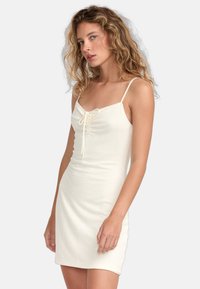 Krämsfärgad bodycon-klänning med tunna axelband, med en samlad front med dragsko, textilier med struktur och en knä-lång nederdel.