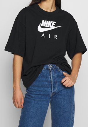 Personne portant un t-shirt noir Nike Air légèrement rentré dans un jean bleu taille haute, debout avec une main dans la poche.