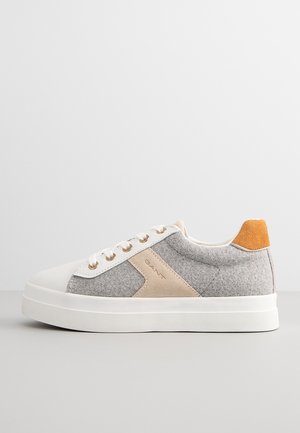 Baskets grises et beiges avec semelle en caoutchouc blanc, présentant un accent en daim orange au talon et des œillets dorés pour les lacets.