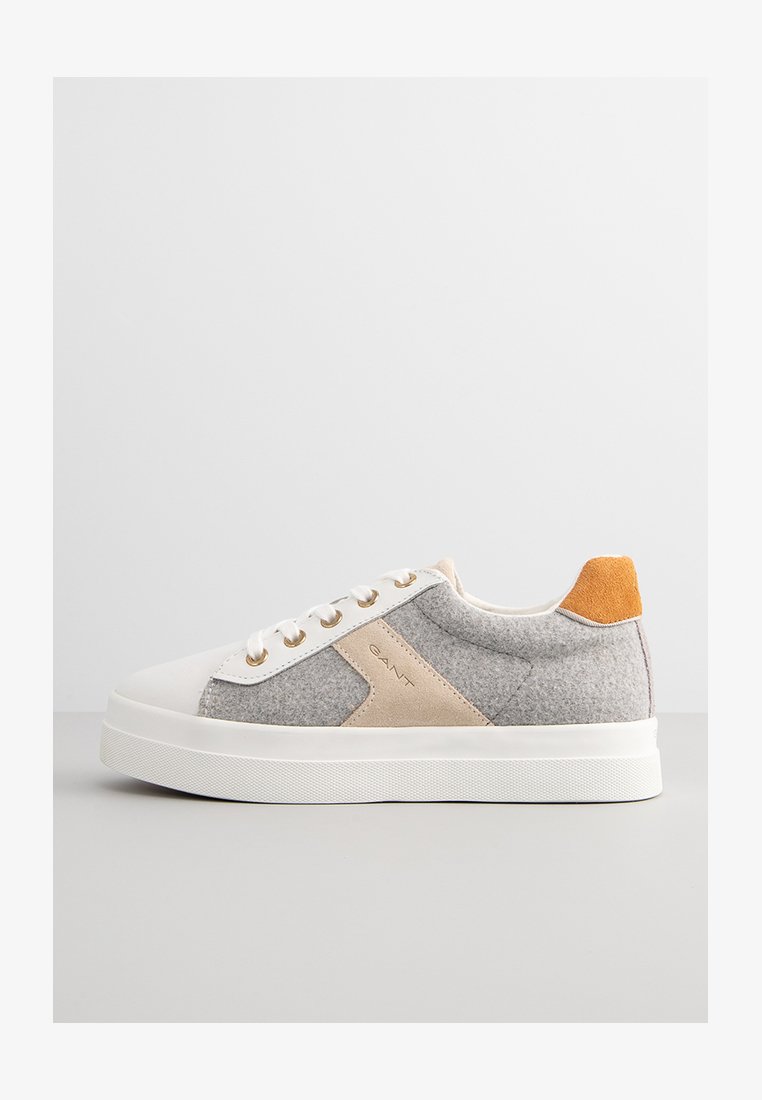 Baskets grises et beiges avec semelle en caoutchouc blanc, présentant un accent en daim orange au talon et des œillets dorés pour les lacets.