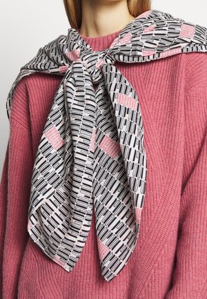 Écharpe noire et rose à motifs nouée autour des épaules sur un pull rose texturé porté par une personne aux cheveux blonds.