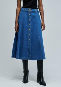 Jeans A-linjekjol i blått, med knappfäste fram, bälte med metallspänne och knä-length design. Slät textur och strukturerad form.