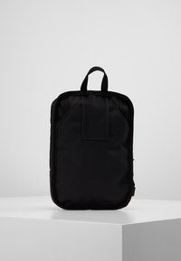 Czarny plecak tekstylny o prostokątnym kształcie, wyposażony w górną pętlę do noszenia, gładką powierzchnię i minimalistyczny design.