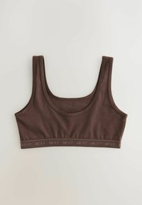 Smeđa crop top braletica izrađena od glatkog materijala. Ima široke naramenice, okrugli izrez i traku s "NEXT" logotipom duž donjeg dijela.