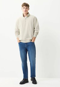 Light beige zip-up sweatshirt, blue denim jeans, and black shoes. Smooth fabric and relaxed fit with ribbed cuffs and collar detail.