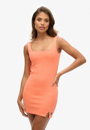 Woman posing in a sleeveless fitted coral dress with square neckline and small side slit against a white background.