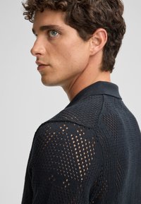 Polo shirt a maglia in navy scuro con un motivo testurizzato di tessitura aperta e sezioni solide, dotato di colletto classico e maniche corte.