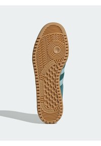 Adidas sneaker outsole with a textured gum rubber bottom, featuring a circular pivot point and herringbone tread pattern for traction.