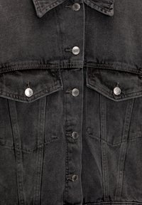 Chaqueta de mezclilla negra con botones a presión plateados, dos bolsillos en el pecho y un acabado texturizado. Diseño clásico de cuello con un ajuste estructurado.