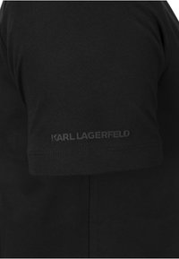 Black cotton T-shirt featuring a short sleeve and a visible "KARL LAGERFELD" logo in black on the lower part of the sleeve.