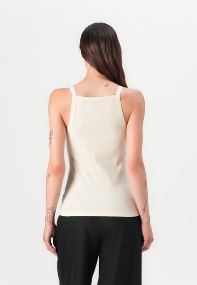 Beige geribbelde tanktop met dunne bandjes, gladde textuur, aansluitend ontwerp en een rechte zoom, gedragen met zwarte broek.