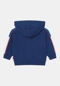 Sudadera azul marino con bolsillo tipo canguro, puños acanalados y rayas en rojo, blanco y azul en los hombros. Tela suave.