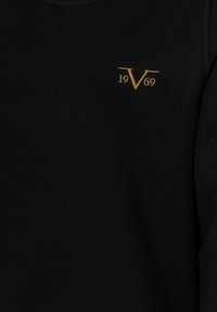 Černá mikina s malým zlatým vyšitým znakem "V" a "1969" na levé horní straně, vyrobená z měkkého bavlněného materiálu.