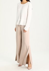 Top bianco a maniche lunghe con orlo a peplum abbinato a pantaloni beige a vita alta e a gamba larga, con spacchi laterali e tessuto morbido.