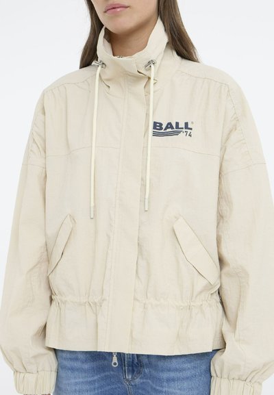 Veste coupe-vent beige avec un col montant, des poches avant, un ourlet élastique et un logo imprimé "BALL 74" sur la poitrine. Tissu texturé.