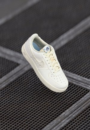 Beež Nike Air Force 1 jooksujalats, millel on perforatsiooniga varvas, lamedad paelad ja tekstuuriga Swoosh logo. Pehme materjal ja pehmendatud sisemus.