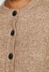 Cardigan en mélange de laine marron avec une finition texturée, un col côtelé et trois boutons noirs sur le devant.
