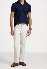 Tmavě modré polo tričko s límečkem, doplněné bílými džínami. Oblečení doplňují hnědé kožené boty a hnědý pásek.