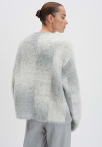 Hellgrauer und weißer karierter Pullover mit einer weichen, flauschigen Textur. Lockerer Schnitt, runder Ausschnitt und Design mit überschnittenen Schultern.