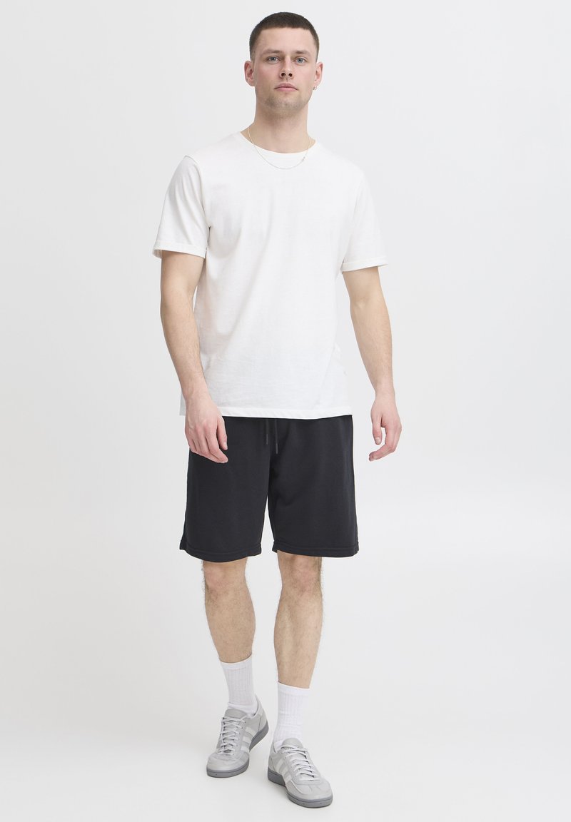 Valge puuvillane T-särk, mida on kombineeritud mustade lühikeste pükstega. Komplekti kuuluvad hallid spordijalatsid ja valged sokid, rõhutades lõdvestunud lõiget ja lihtsat disaini.