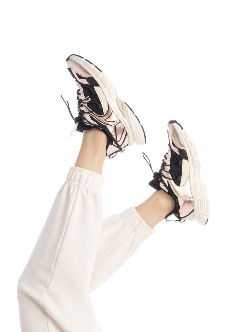 Las zapatillas chunky tienen una parte superior de malla negra con acentos metálicos en rosa, suelas de goma blanca y cordones negros en contraste. Diseño de tacón elevado.