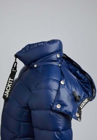 Veste d'hiver matelassée bleue avec col montant et capuche amovible, équipée de sangles noires à logo et de boutons-pression argentés.