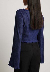 Navyblauw geplooid top met lange klokmouwen, textuurstof, een aansluitende taille en een gegolfde zoom, gecombineerd met zwarte broek.