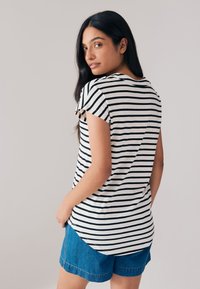 Randig t-shirt med kort ärm i vitt och svart, med rundad nederkant och avslappnad passform. Kombinerad med denimshorts.