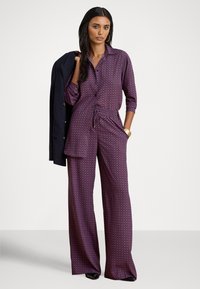 Lilla mønstret jumpsuit med knappeskjorte-design, midjebånd og vide ben. Har en avslappet passform og teksturert stoff.