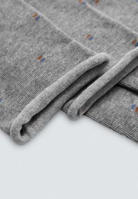 Calcetines de punto grises con un puño enrollado, con pequeños puntos azules y naranjas dispersos por la tela. Textura suave y diseño versátil.