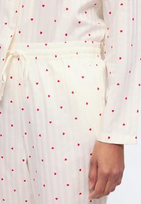 Σετ λευκή πυτζάμα με μικρά κόκκινα μοτίβα καρδιάς, ελαστική μέση με κορδόνι και μανίκι με μανσέτα, άνετη εφαρμογή.