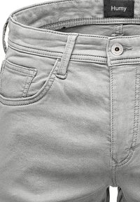 Graue Denim-Jeans mit glatter Textur, standardmäßiger Knopfverschluss, Fünf-Taschen-Design und einem Markenlabel am Bund.