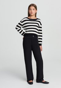 Maglione a righe bianche e nere con scollo largo e orlo a coste. Abbinato a pantaloni neri a gamba dritta e ballerine nere.