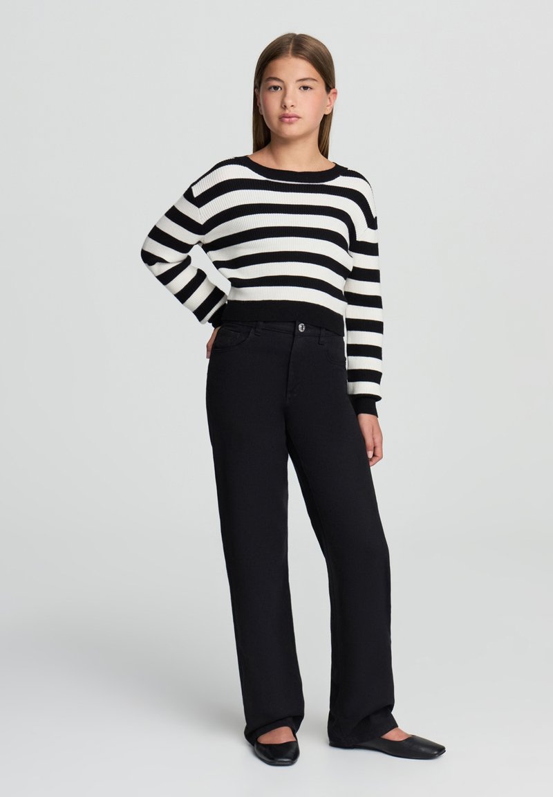 Maglione a righe bianche e nere con scollo largo e orlo a coste. Abbinato a pantaloni neri a gamba dritta e ballerine nere.