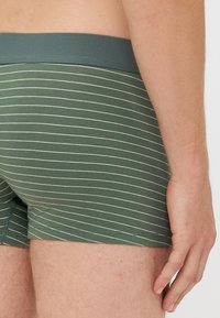 Boxers rayés vert et blanc avec une taille élastique douce et une coupe ajustée, présentant une texture de tissu lisse.