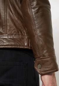 Bruine leren jacket met een gestructureerde afwerking, opvallende stiksels en knoopmanchetten. Het ontwerp is uitgerust met een slank silhouet.