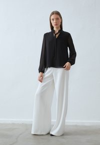 Zwarte blouse met een gerimpelde kraag en strikdetail, gecombineerd met hoogwaisted, wijdvallende witte broeken. Glad stoffen met contrasterende kleuren.