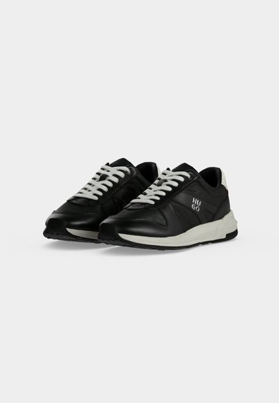 Paire de baskets en cuir noir avec lacets et semelles blancs, affichant le logo "HUGO" sur le côté, sur fond blanc.