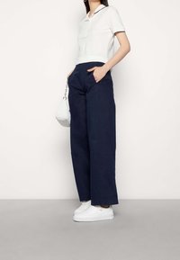 Marinblå vida byxor med framfickor, kombinerade med en vit polo med marinblå krage. Bärs med vita platåskor.