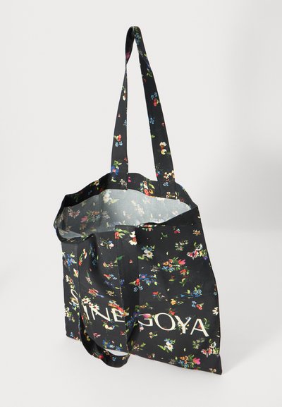 Geantă tote neagră cu un model floral multicolor, două mânere lungi, vârf deschis și un logo alb al mărcii pe față. Textură de țesătură fină.