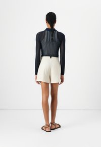 Marineblauwe top met lange mouwen en geribbelde textuur, gecombineerd met lichtbeige, op maat gemaakte shorts. Model draagt bruine sandalen. Schoon, modern ontwerp.