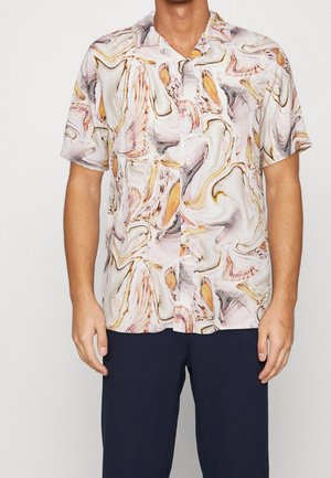 Mand iført en kortærmet skjorte med knapper og et abstrakt mønster af hvide, orange og grå skaller samt mørke bukser.