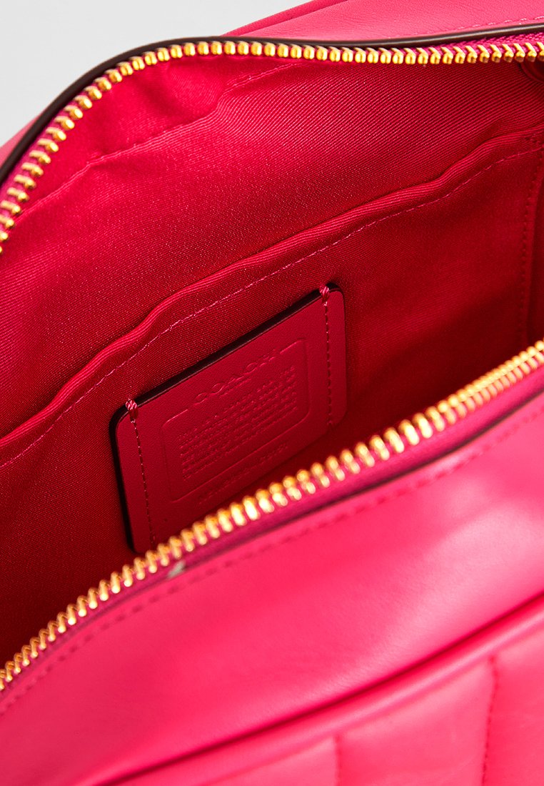 Lys rosa läderväska inuti med en gulddragkedja, tygfoder och en präglad varumärkesetikett i en sidoficka.