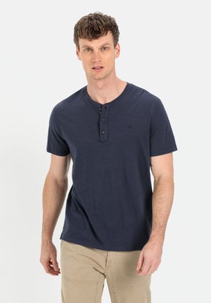 Marineblå t-shirts med korte ærmer og henley-udskæring, rund hals, tre-knap lukning og diskret logo-detalje på brystet. Blødt, struktureret stof.